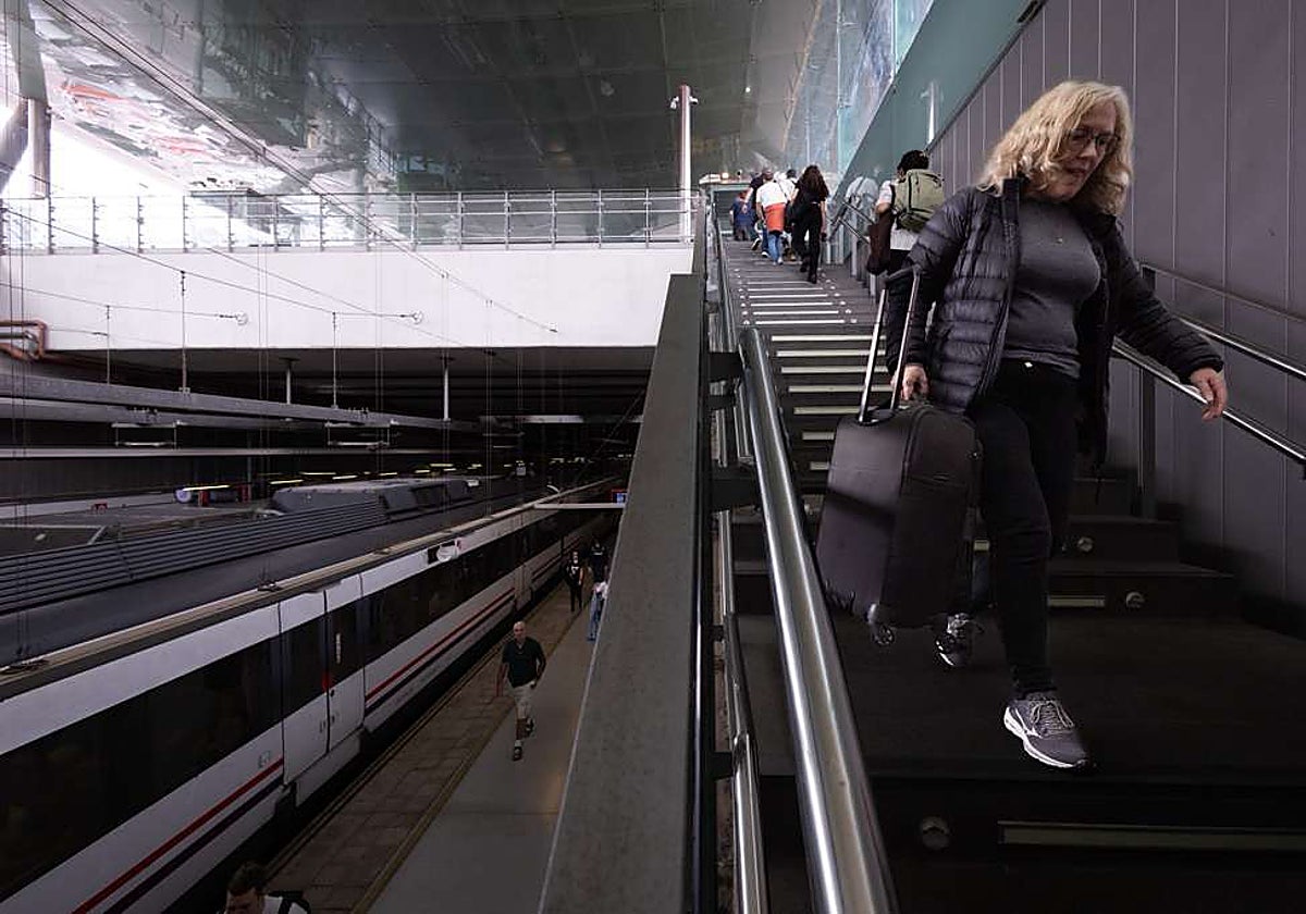 Una viajera baja por las escaleras en la estación, a pie con la maleta a cuestas.