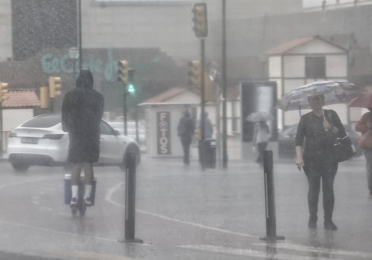 Un hombre circula en patinete bajo la lluvia en el entorno de El Corte Inglés de Málaga.