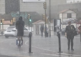 Un hombre circula en patinete bajo la lluvia en el entorno de El Corte Inglés de Málaga.