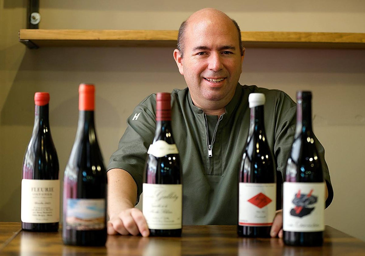 Imagen principal - Arriba, el sumiller junto a una muestra de algunas de sus botellas. Abajo, tartar de atún con gazpachuelo y vieira con gazpacho de naranja. 