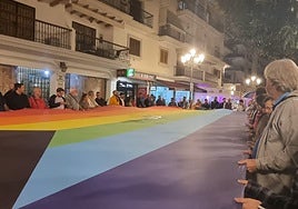 Participantes en la concentración con una gran bandera LGTBIQ+.