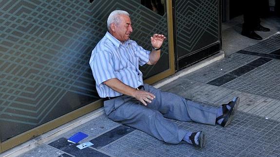 Giorgos Shatzifotiadis llora desconsolado a la puerta de un banco. 