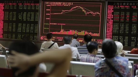 Inversores chinos sentados ante unas pantallas que muestran datos bursátiles. 