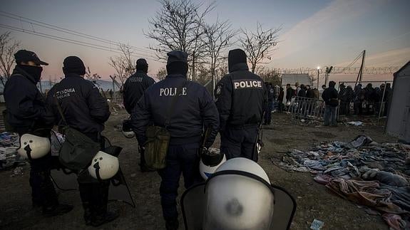 Policías vigilan a un grupo de refugiados en un campo de Idomeni, Grecia.