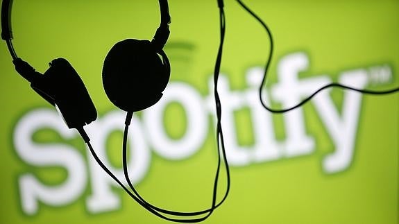 Unos auriculares frente al logotipo de Spotify. 