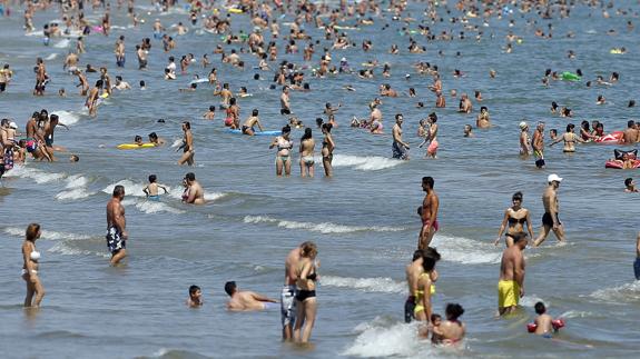 Un gran número de personas disfrutan del buen tiempo estival en la playa de la Malvarrosa.