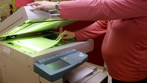 Una mujer embarazada hace fotocopias en la oficina.