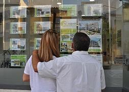 Una pareja consulta las ofertas de viviendas que cuelgan del escaparate de una inmobiliaria.:: A. Peláez