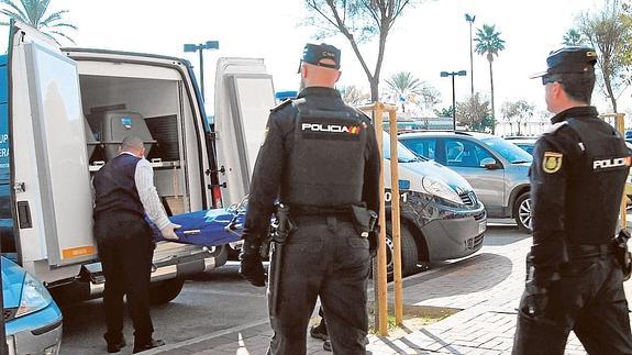 Operarios de la funeraria judicial retiran el cadáver ante la mirada de unos policías. 