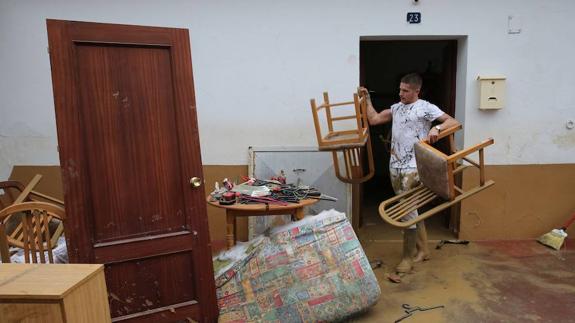 Un vecino afectado por las inundaciones en Cártama retira enseres mojados de una casa. 