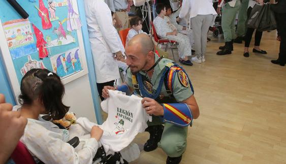 Un legionario se agacha para ponerse a la altura de una pequeña, a la que le regala una camiseta de la Legión Española.