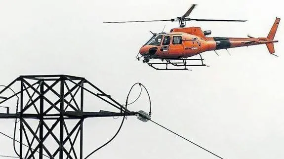 Imagen de archivo de un helicóptero de la compañía realizando tareas junto a una torre de alta tensión.