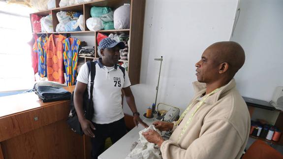 Ibrahima Balde, de la ONG Accem, conversa con el propietario de una tienda de costura.