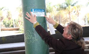 LIMPIEZA. La concejala Teresa Porras coloca en una farola una pegatina informativa sobre la campaña. / SUR
