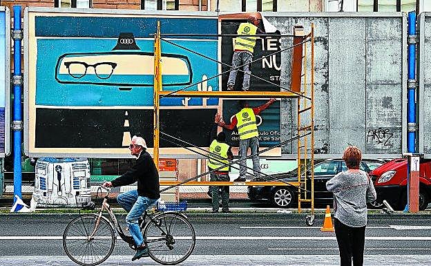 Un ciclista pasa ante los paneles de la Zurriola, junto al Kursaal, mientras los operarios colocan los carteles de las películas.