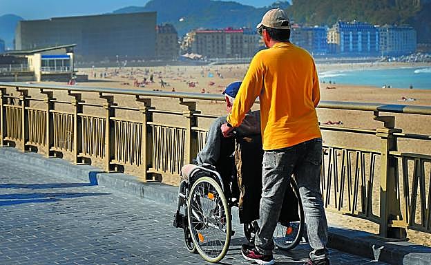 Un hombre pasea a una persona en silla de ruedas por la Zurriola en Donostia.