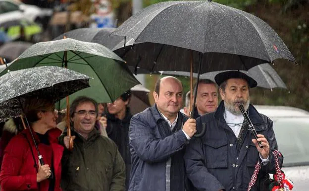 El presidente del PNV, Andoni Ortuzar (c) tapa con su paraguas a un txistulari después de salir de la misa de homenaje a Sabino Arana. Detrás de ellos, el Lehendakari Iñigo Urkullu. 