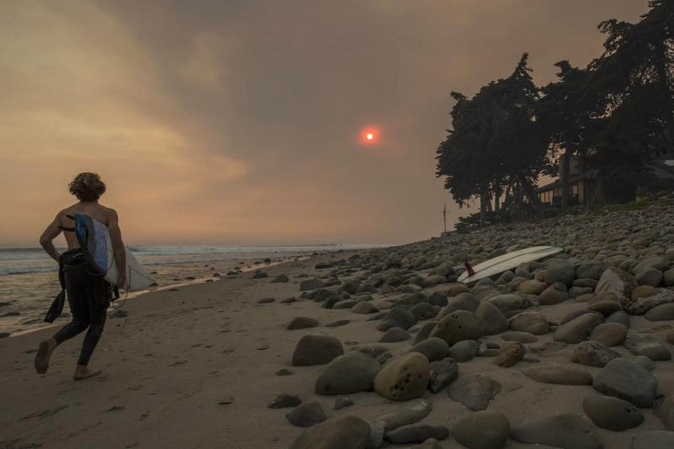 Un cielo lleno de humo alrededor de los surfistas. El fuego continúa creciendo y amenaza a las comunidades desde Carpinteria hasta Santa Barbara, California. El incendio se ha extendido a lo largo de 365 millas hasta el momento y ha destruido unas 800 estructuras desde que comenzó el 5 de diciembre en Ojai, California.