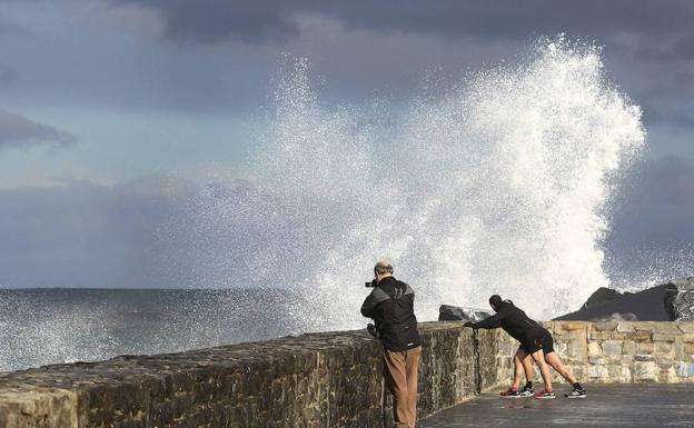 Una persona fotografía una ola que salta por encima del espigón de la playa de La Zurriola. 