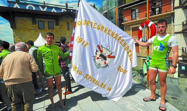 Los remeros de Hondarribia Gonzalo Carrión y Beñat Egiazu sostienen la bandera que les fue entregada en tierra. 