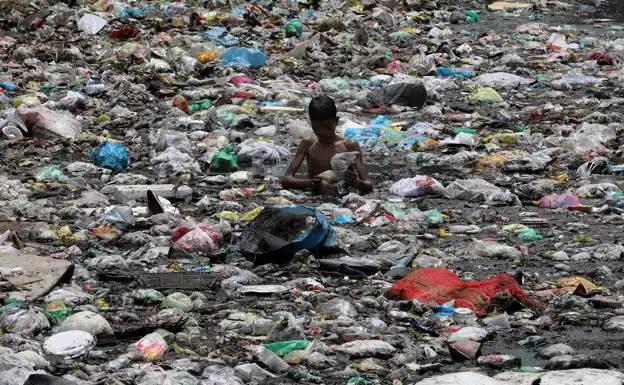 Un niño busca material reciclable entre la basura que flota en un canal de India