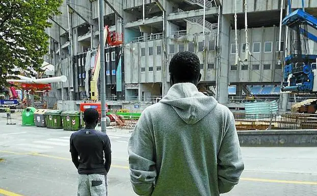 Dos de los migrantes contemplan las obras del estadio de Anoeta. 