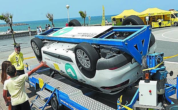 Dos personas con un voluntario de la DYA junto al simulador de vuelco de coche