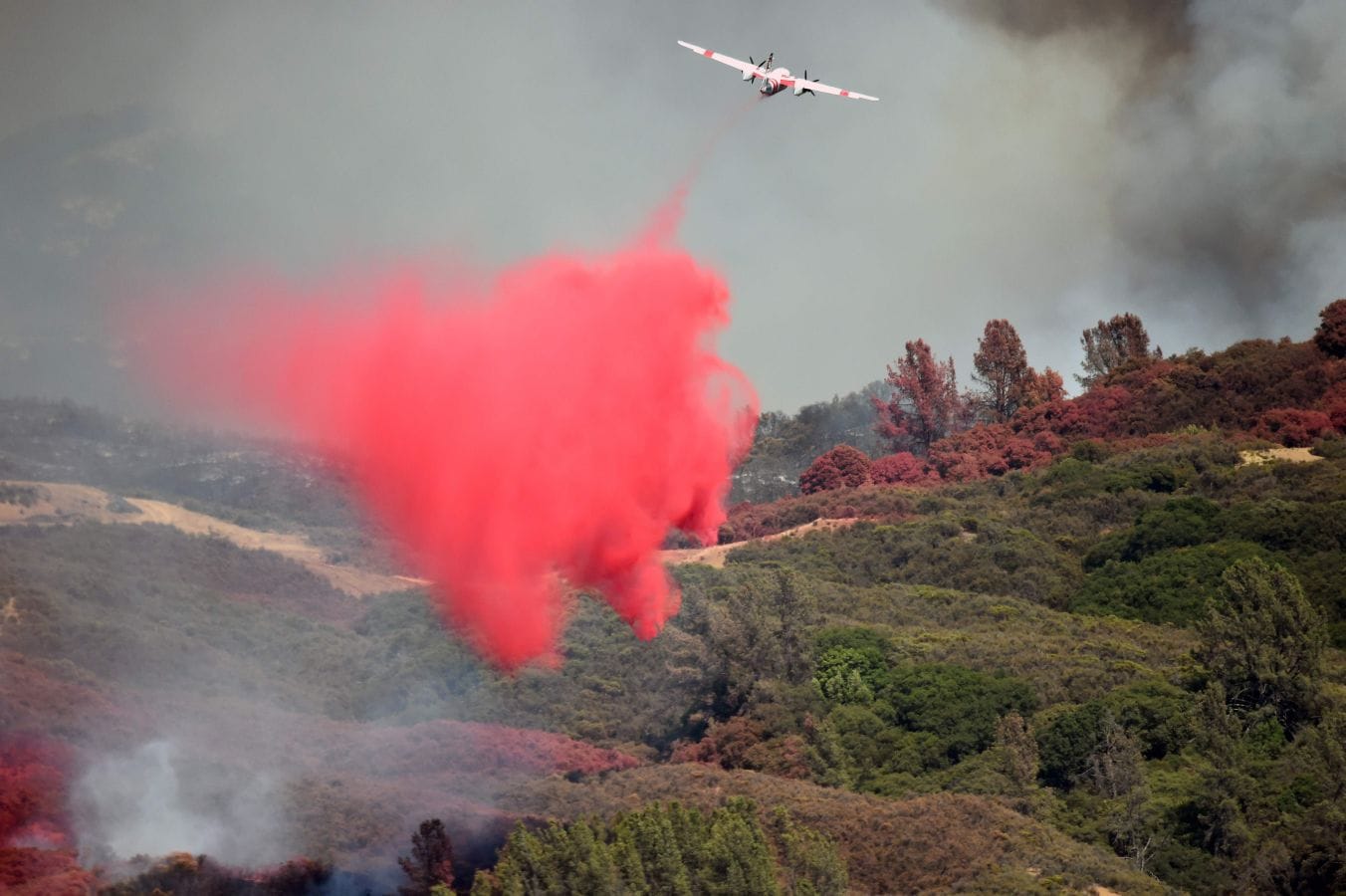 Un avión expulsa retardante rojo para frenar el fuego