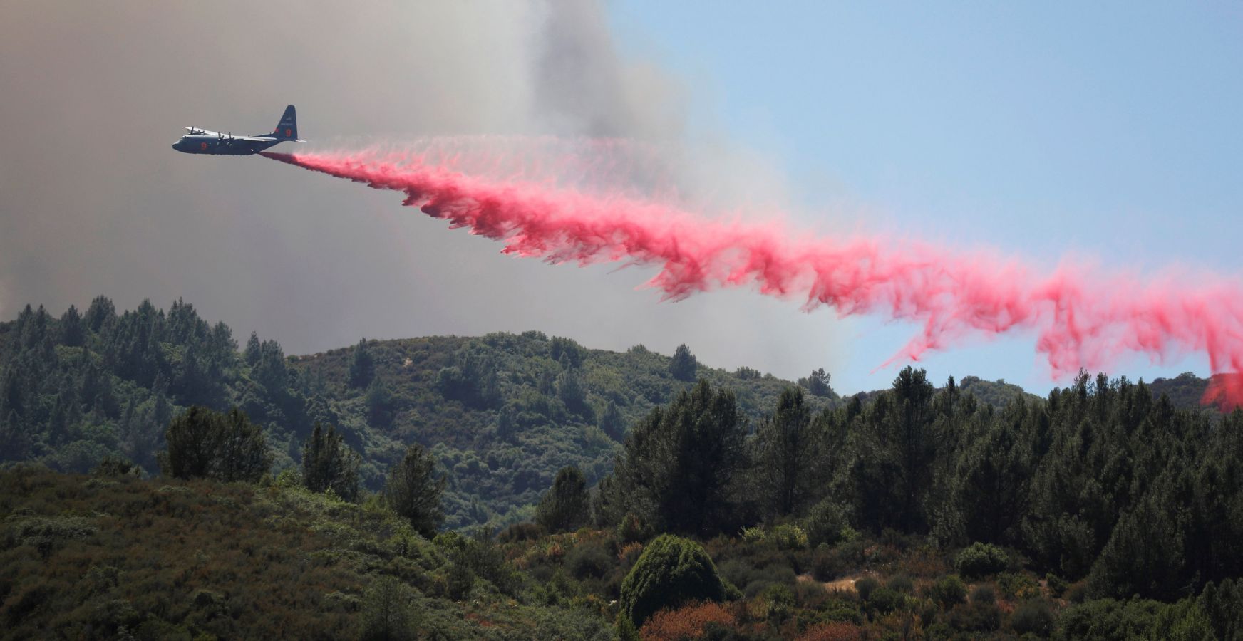 Un avión expulsa retardante rojo para frenar el fuego