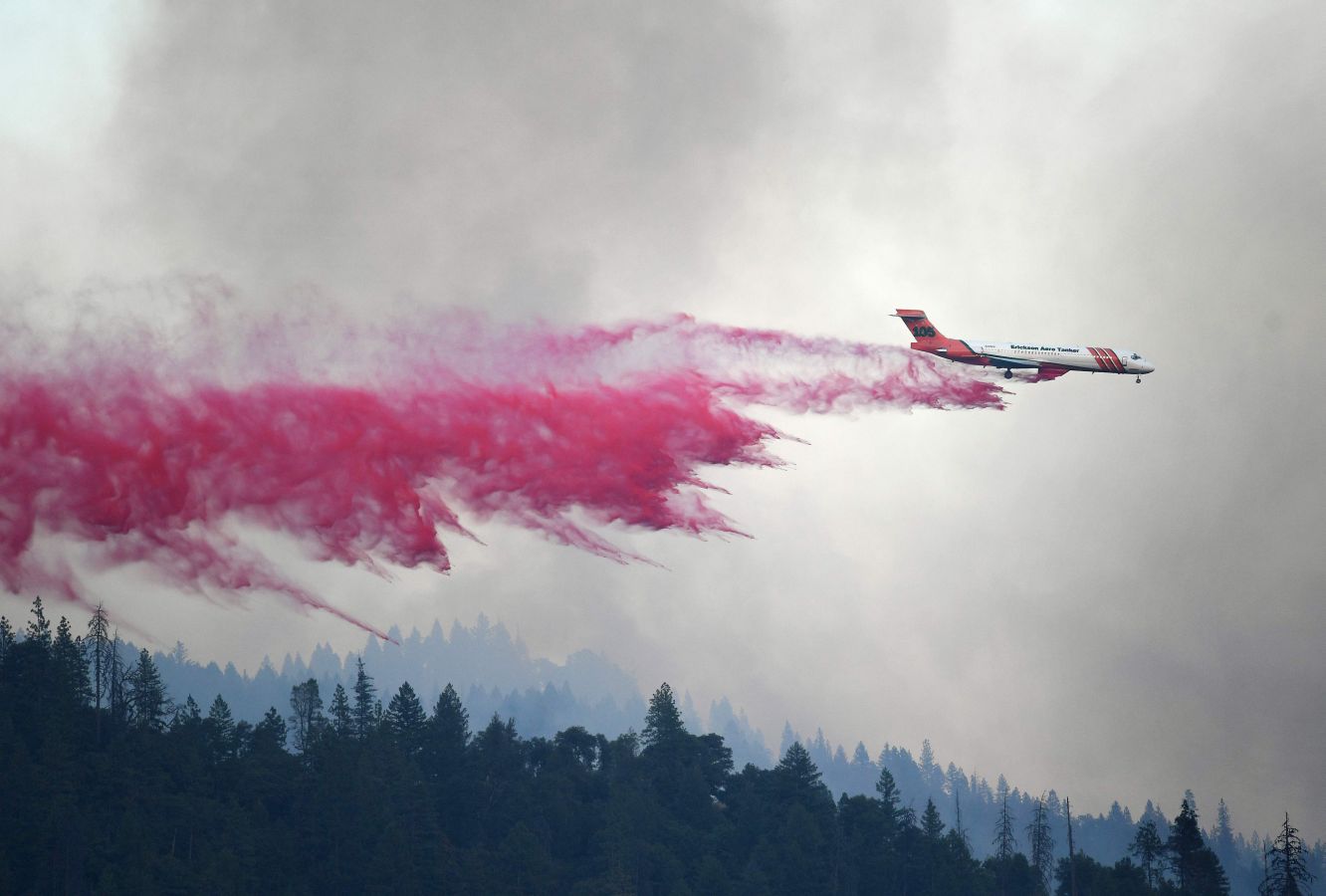 Un avión expulsa retardante rojo para frenar el fuego