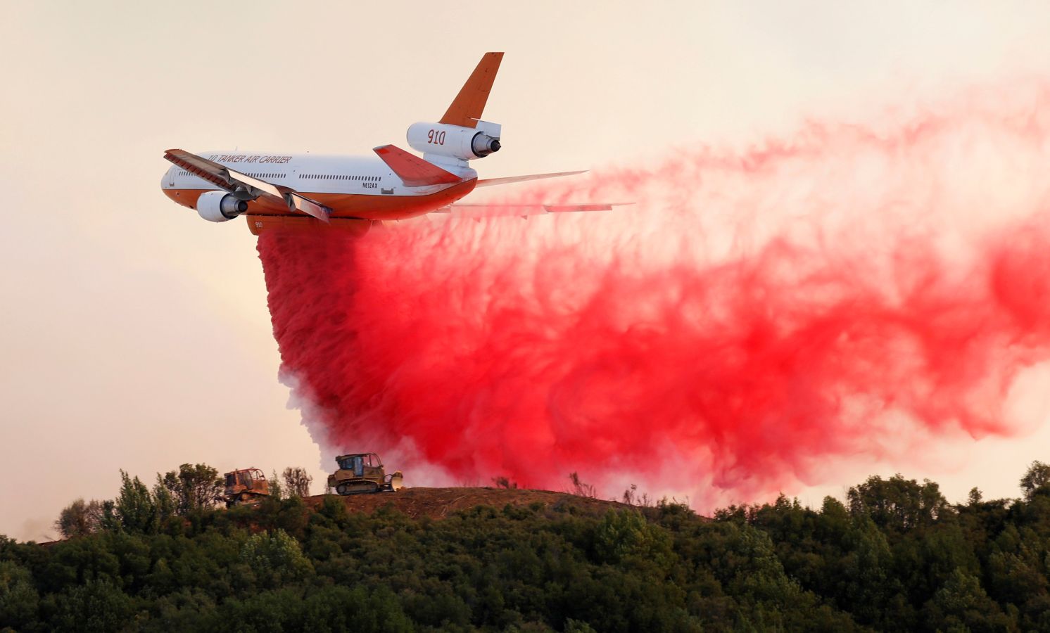 Un avión expulsa retardante rojo para frenar el fuego