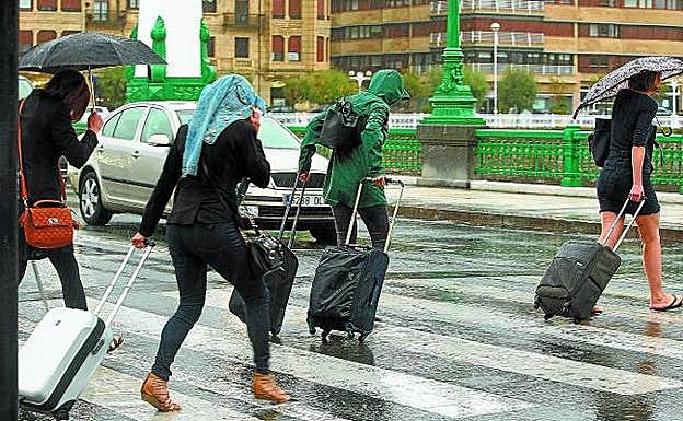 Con sandalias y bajo el paraguas. Así se fueron ayer los turistas que han pasado el puente en Gipuzkoa, a los que sorprendió la lluvia después de un sábado de calor.