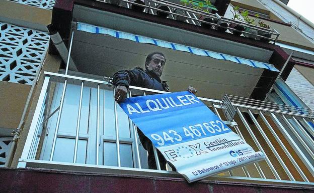 Un experto inmobiliario coloca un cartel de alquiler en un piso de San Sebastián. 