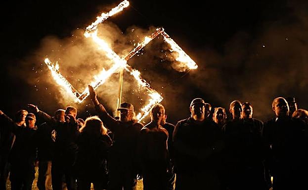 Neonazis estadounidenses hacen el saludo fascista delante de una cruz gamada en llamas en Virginia (EE UU).