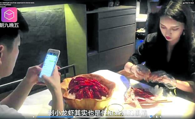 Una estudiante pela cangrejos para un cliente atento al móvil en uno de los vídeos de promoción del restaurante.