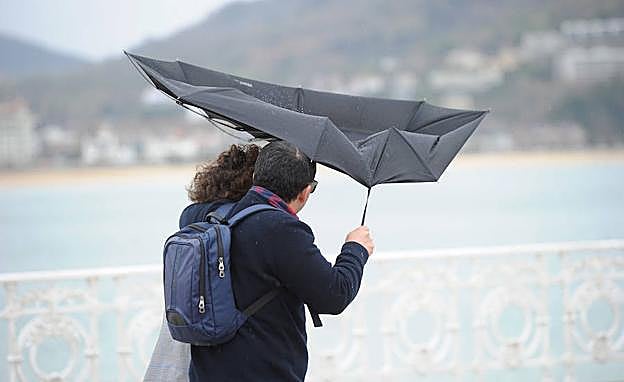 Una pareja pasea por San Sebastián y se protege de la lluvia y el viento con un paraguas.