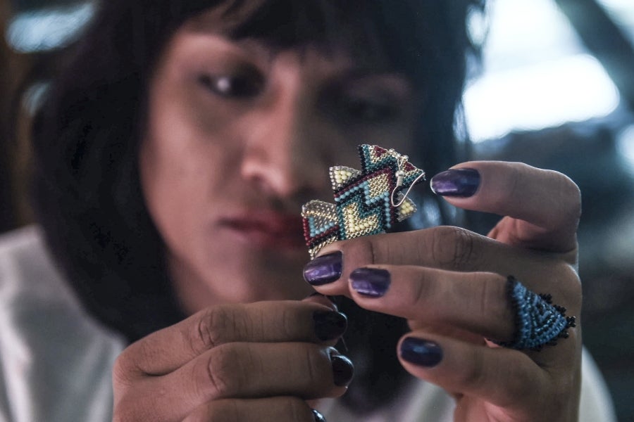 La colombiana Roxana Panchi Gutiérrez, una joven transexual indígena de 24 años, se reúne con sus dos amigas de toda la vida, en el pueblo indígena Cristiania, departamento de Antioquia, para crear accesorios con cuentas. Las mismas cuentas que iluminan las últimas creaciones de la diseñadora colombiana Laura Laurens, cuyos diseños viajan desde Bogotá a Londres, París y Nueva York.