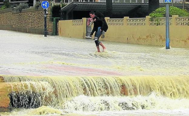 Dos jóvenes intentan cruzar una calle en Benidorm en medio de un torrente de agua espontáneo creado por las fuertes lluvias. 