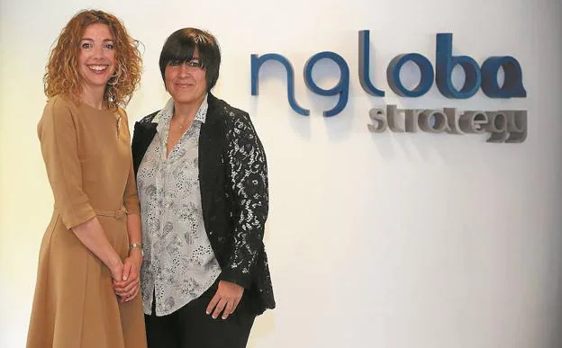Iratxe Pascual y Virginia Amilibia posan junto al logo de su empresa, nGloba, en la oficina de San Sebastián.