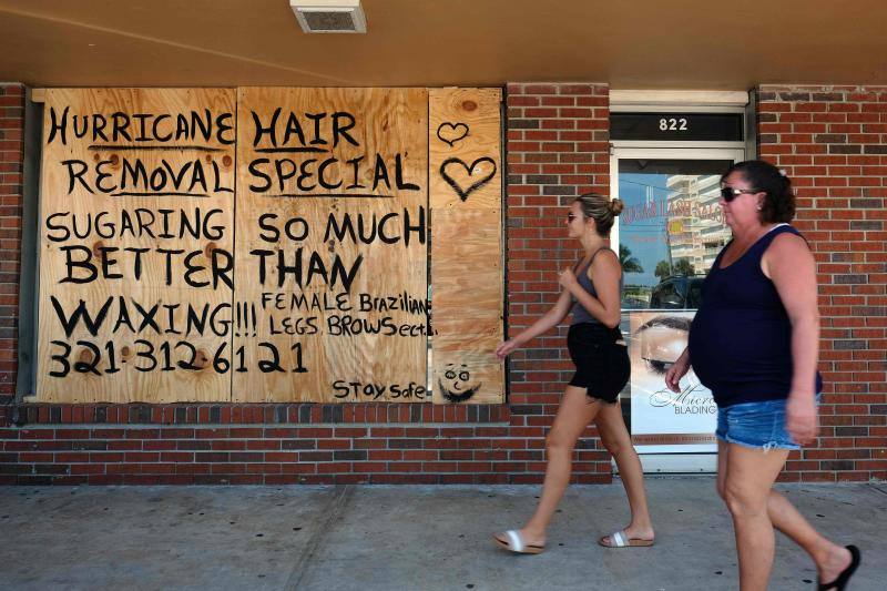 Dos mujeres pasean por Cocoa Beach, en Florida, frente a un comercio apuntalado.