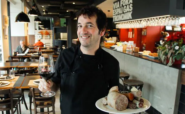Ander Echebarria, jefe de cocina del Via Fora, posa con una copa de vino y un plato de productos de gastronomía catalana.