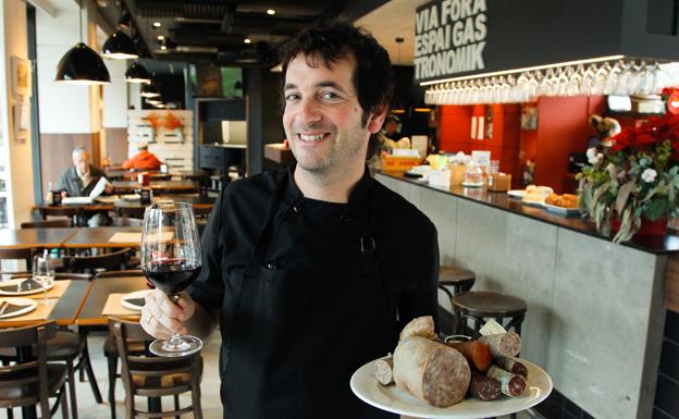 Ander Echebarria, jefe de cocina del Via Fora, posa con una copa de vino y un plato de productos de gastronomía catalana.