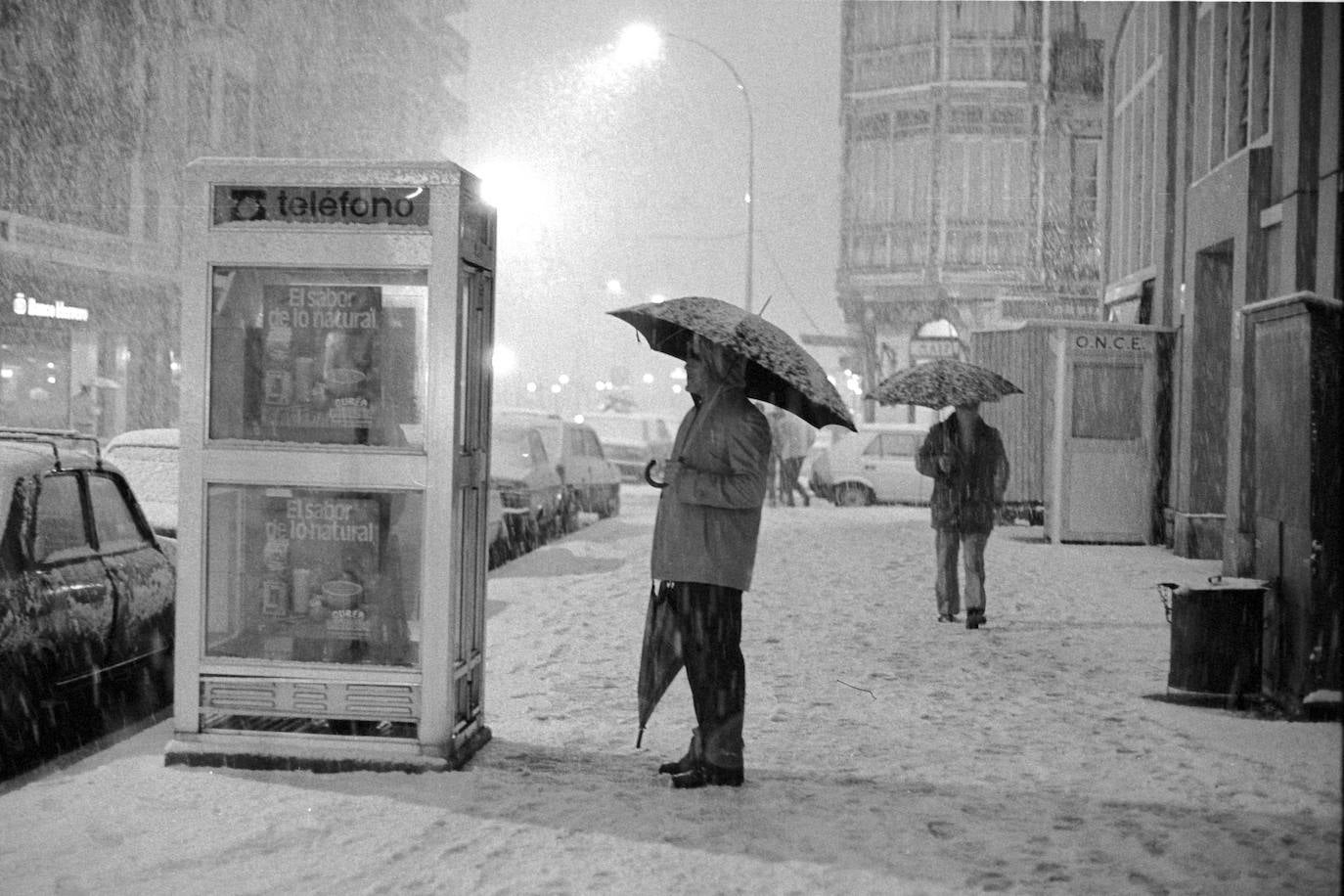 Un hombre espera bajo la nevada ante una cabina telefónica en la acera del Mercado San Martín de la calle Urbieta de San Sebastián 
