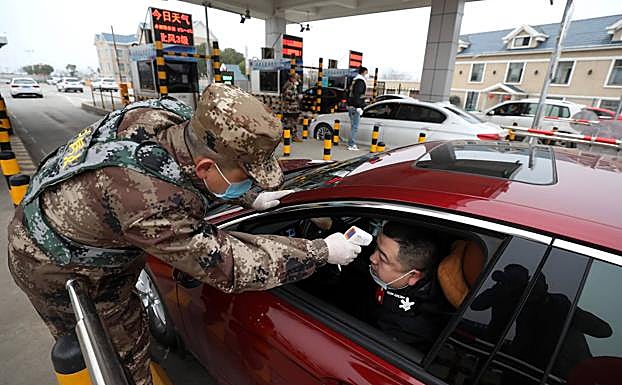 Un miembro del Ejército controla la temperatura corporal de un conductor en el peaje de una autopista en Wuhan.