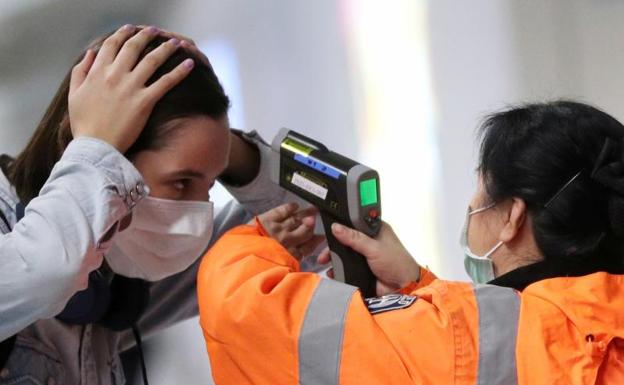 Una agente toma la temperatura a una pasajera en el aeropuerto de Hong Kong.