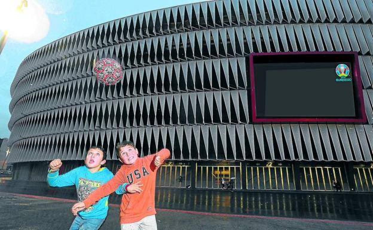 Unos niños juegan con el balón en las inmediaciones de San Mamés; en la pantalla del estadio se han incluido los partidos que se disputarán en La Catedral.