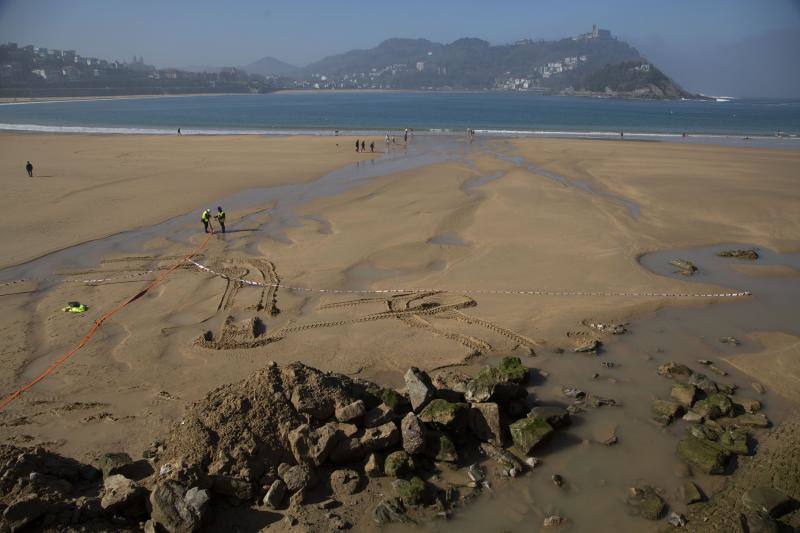 La playa de La Concha se ha convertido en la bajamar de este lunes por la mañana en un inesperado yacimiento arqueológico. La presencia de una pequeña excavadora retirando piedras y escombros junto al muro de costa a la altura del edificio consistorial ha suscitado una gran expectación entre los numerosos viandantes y turistas que han provechado el buen tiempo para dar un paseo. La máquina profundizaba en la arena en busca de los restos de un barco hundido del que hay constancia documental desde el siglo XVIII. 