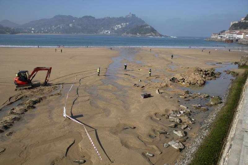 La playa de La Concha se ha convertido en la bajamar de este lunes por la mañana en un inesperado yacimiento arqueológico. La presencia de una pequeña excavadora retirando piedras y escombros junto al muro de costa a la altura del edificio consistorial ha suscitado una gran expectación entre los numerosos viandantes y turistas que han provechado el buen tiempo para dar un paseo. La máquina profundizaba en la arena en busca de los restos de un barco hundido del que hay constancia documental desde el siglo XVIII. 