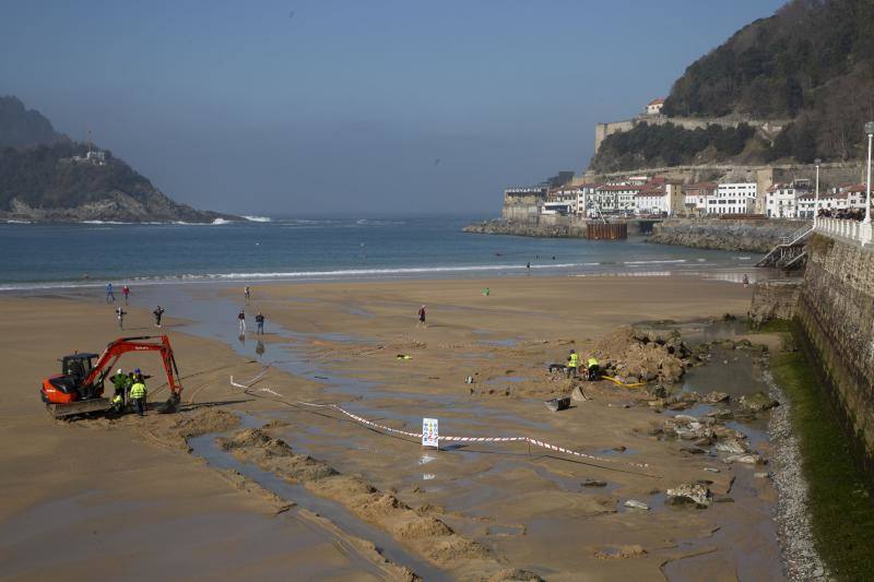 La playa de La Concha se ha convertido en la bajamar de este lunes por la mañana en un inesperado yacimiento arqueológico. La presencia de una pequeña excavadora retirando piedras y escombros junto al muro de costa a la altura del edificio consistorial ha suscitado una gran expectación entre los numerosos viandantes y turistas que han provechado el buen tiempo para dar un paseo. La máquina profundizaba en la arena en busca de los restos de un barco hundido del que hay constancia documental desde el siglo XVIII. 