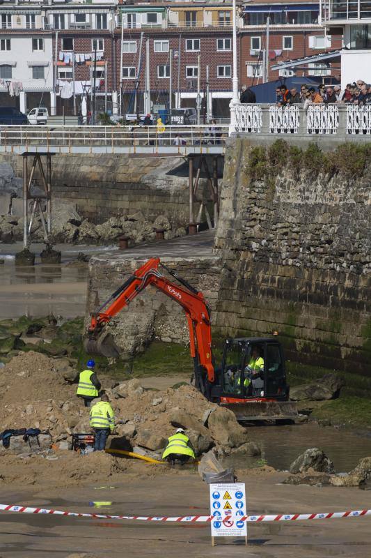 La playa de La Concha se ha convertido en la bajamar de este lunes por la mañana en un inesperado yacimiento arqueológico. La presencia de una pequeña excavadora retirando piedras y escombros junto al muro de costa a la altura del edificio consistorial ha suscitado una gran expectación entre los numerosos viandantes y turistas que han provechado el buen tiempo para dar un paseo. La máquina profundizaba en la arena en busca de los restos de un barco hundido del que hay constancia documental desde el siglo XVIII. 